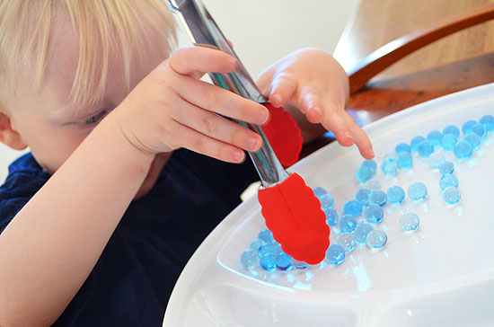 child pick up marbles with tongs