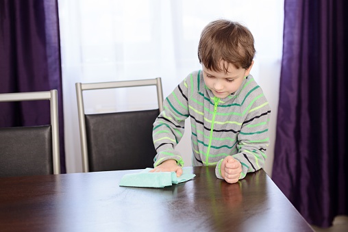 Boy child cleaning table in kitchen with rag.