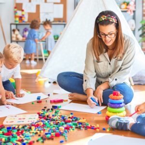 Beautiful teacher and group of toddlers playing around lots of toys at kindergarten